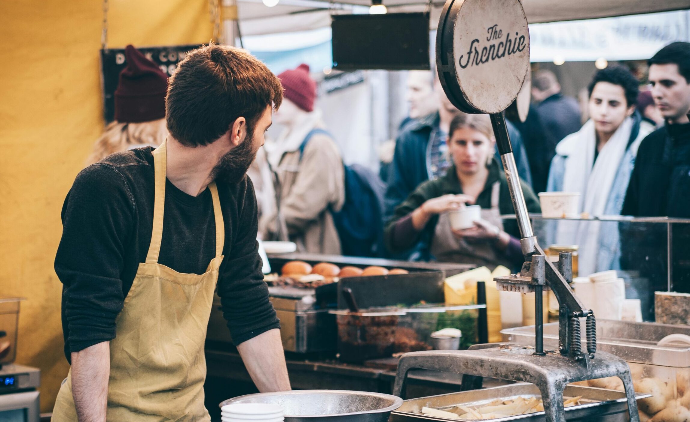 Cena dinâmica de um vendedor de comida de rua trabalhando em um mercado movimentado, interagindo com clientes diversos.