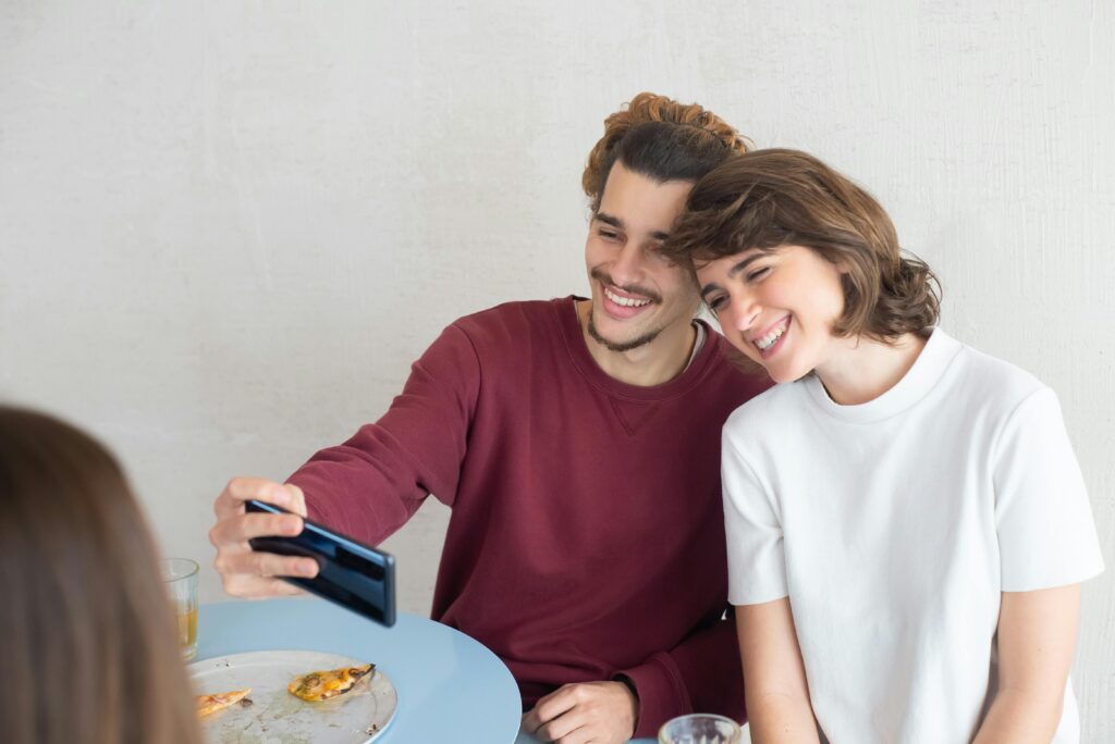 Happy couple taking a selfie at a cafe table with pizza slices.