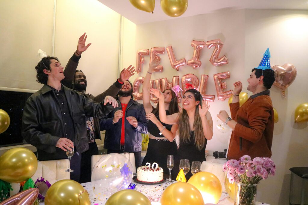 Group of friends celebrating a birthday indoors with balloons and cake.